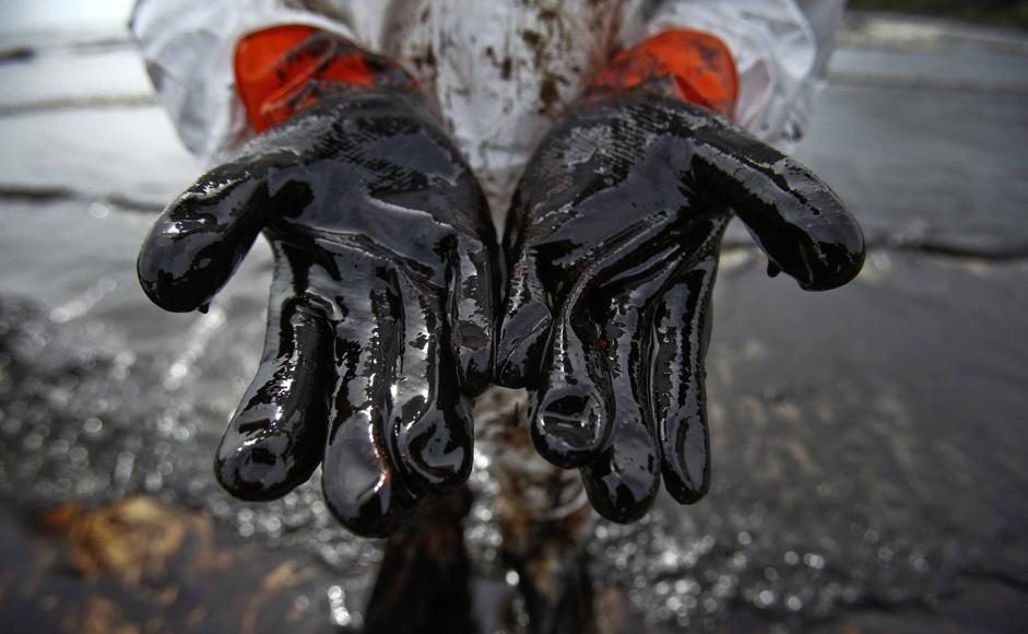 A Thai soldiers shows his glove covered with oil slick during a clean-up operation at Ao Prao Beach on Koh Samet